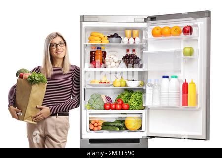 Junge Frau mit einer Einkaufstasche, die sich auf einen Kühlschrank lehnt, isoliert auf weißem Hintergrund Stockfoto