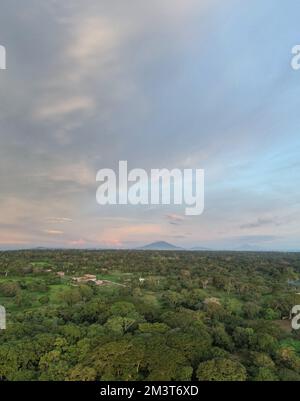 Grüne Landschaft mit Vulkan auf pinkfarbenem Sonnenuntergang am Himmel Stockfoto