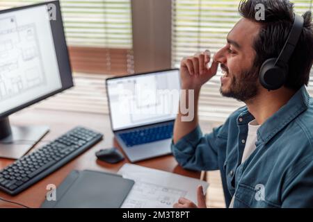 Lächelnder indischer Designer in Kopfhörern arbeitet im Home Office und zeichnet auf einem Grafiktablett Stockfoto