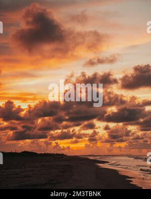 Ein Sonnenuntergang über dem Strand mit bewölktem und feurigem Hintergrund Stockfoto