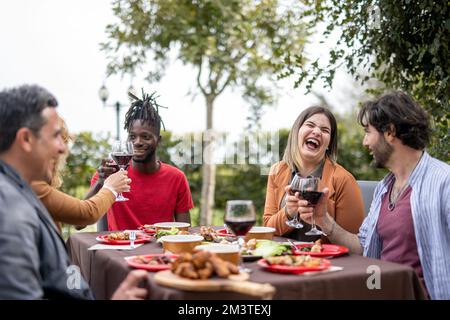 Glückliche Menschen, die sich im Garten beim Essen und Trinken von Wein amüsieren, Diversität und gemischte Altersgruppen Konzept Stockfoto