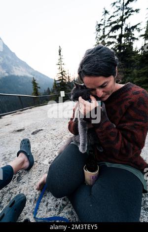 Die junge weiße 30s-jährige Frau hält ihre graue russische blaue Katze und schenkt ihre Liebsten draußen im Wildnis-Wald, während sie mit ihrem Mann auf einer beliebten Straße unterwegs ist Stockfoto