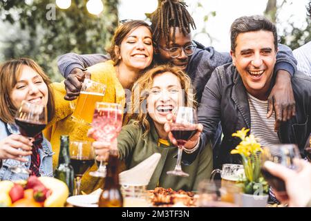 Gruppe mit lächelnden Freunden, die auf einer privaten Party trinken und anstoßen, Leute, die Spaß im Freien haben, Familientreffen, Happy Hour Stockfoto