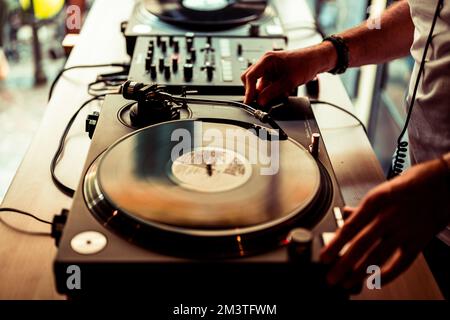 DJ-Hände auf dem Gerätedeck und Mixer mit Schallplatte auf der Party, menschliche Hände mit zwei Vinyl-Drehtisch-Spielern, die nacheinander Lieder spielen. Stockfoto