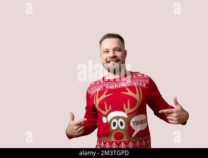 Junger, bärtiger Mann, der seinen Rentier-Weihnachts-Pullover zeigt, isoliert auf rotem Hintergrund. Speicherplatz kopieren Stockfoto