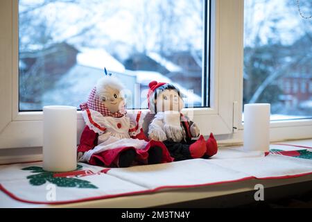 Die Puppe im Weihnachtsstil sitzt mit Kerzen auf einem Fensterbrett. Stockfoto