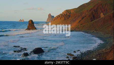 Große Wellen mit Schaumstoffrollen am hügeligen Ozean Felsenstrand bei Sonnenuntergang. Relax 4K Genießen Sie den Landschaftsblick. Teneriffa, Kanarische Inseln, Spanien Stockfoto