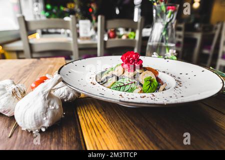 Schwarze Tagliolini-Pasta mit Garnelen, serviert auf einem dunkelweißen Teller. Restaurantinnenausstattung. Essbare Blüten als Dekoration für Lebensmittel. Hochwertiges Foto Stockfoto