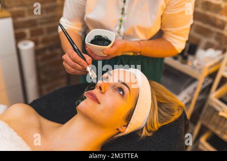 Nahaufnahme einer hübschen jungen Frau, die im Schönheitszentrum eine Maske bekommt, Gesichtsbehandlung. Hochwertiges Foto Stockfoto