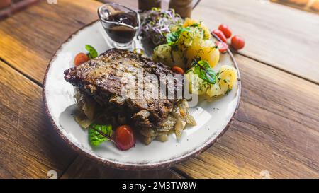 Traditionelles polnisches Fleischgericht: Schweinerippchen mit gekochten Kartoffeln und Gemüse der Saison. Holztisch als Hintergrund. Hochwertiges Foto Stockfoto