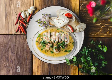 Meeresfrüchte-Gericht. Garnelen in scharfer Sauce gekocht mit drei Brotstücken auf weißem Teller. Dekoration von Petersilie, Knoblauchzehen und Chili-Paprika. Hochwertiges Foto Stockfoto