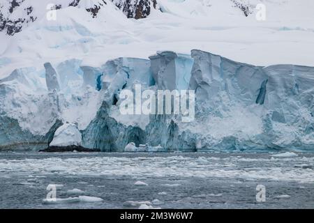 Zerklüftete blaue Eisbildung am Rande der antarktischen Halbinsel. Schnee und Felsen im Hintergrund; ruhiges Meer, übersät mit Seeis. Stockfoto