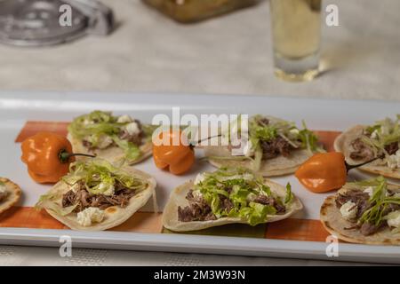 Nahaufnahme von Chalupas, typisches mexikanisches Gericht mit Tortillas, Sauce, Käse, Fleisch und Salat auf weißer Tischdecke Stockfoto