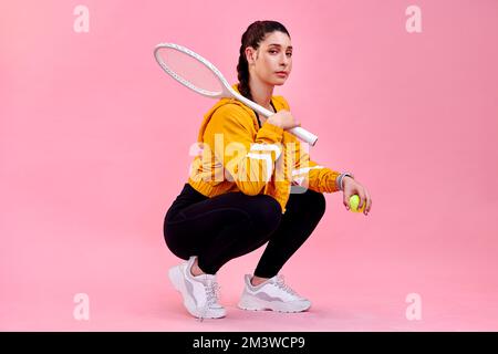Ich überlasse dem Schläger das Reden. Studioporträt einer sportlichen jungen Frau, die mit einem Tennisschläger und einem Ball vor pinkfarbenem Hintergrund posiert. Stockfoto