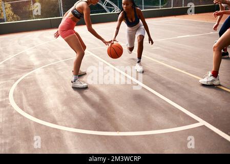 Immer den Ball schützen. Eine vielfältige Gruppe von Sportlerinnen, die tagsüber gemeinsam ein Wettkampfspiel mit Basketball spielen. Stockfoto