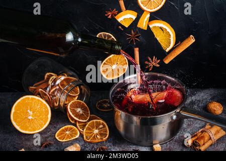 Glühweinzutaten, Zitrusfrüchte, Zimt und Sternanis fliegen aus der Höhe und sorgen für Spritzer. Ein Kessel Glühwein, in den fr Stockfoto