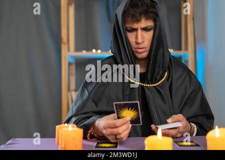 Ein Wahrsager, der Tarot-Karten auf einem Tisch mit Kerzen liest. Stockfoto