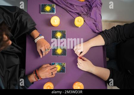 Ein Wahrsager, der Tarotkarten in der Hand hält, und eine nicht wiedererkennbare Frau, die die Karte auswählt. Stockfoto