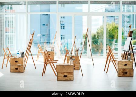 Beginnen Sie jeden Tag mit einer leeren Leinwand. Eine Gruppe Staffeleien und Leinwände in einem leeren Kunststudio vor einem Malkurs. Stockfoto