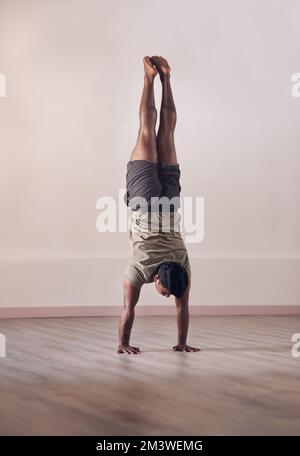 Das Gleichgewicht ist in jedem Lebensbereich von entscheidender Bedeutung. Die volle Länge eines sportlichen jungen Mannes, der einen Handstand im Studio macht. Stockfoto