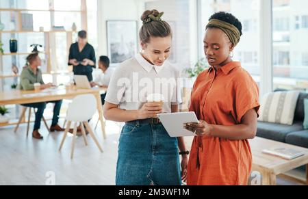 Ich dachte, wir könnten das machen. Zwei attraktive junge Geschäftsfrauen stehen zusammen und diskutieren im Büro. Stockfoto