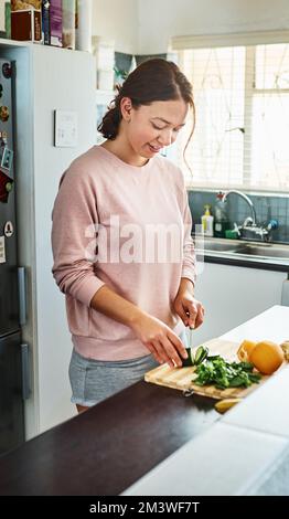 Beginnen Sie jetzt gesund zu essen. Eine junge Frau, die zu Hause in der Küche Gemüse hackt. Stockfoto