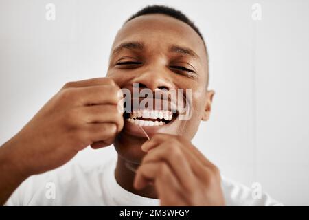 Zahnseide ist genauso wichtig. Ein junger Mann, der sich zu Hause im Bad die Zähne mit Zahnseide reinigt. Stockfoto