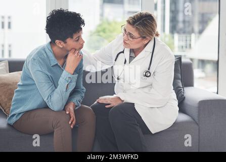 Sie werden dies überwinden... eine mitfühlende junge Ärztin, die eine Patientin tröstet, während sie in ihrem Büro auf der Couch sitzt. Stockfoto