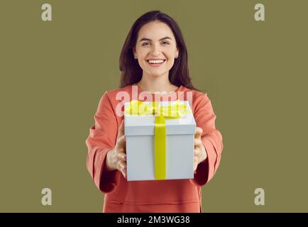 Eine lächelnde braune Frau in rotem Sweatshirt schenkt ein Geschenk, das Hände auf Khaki-Hintergrund zieht. Stockfoto
