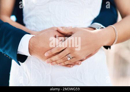 Er machte sie zu seiner Frau. Ein unbekannter Bräutigam umarmt seine Braut von hinten, während er an ihrem Hochzeitstag draußen steht. Stockfoto