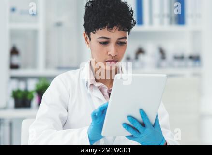 Drahtlose Technologie trifft Biotechnologie. Eine attraktive junge Wissenschaftlerin, die während der Arbeit im Labor ein digitales Tablet verwendet. Stockfoto