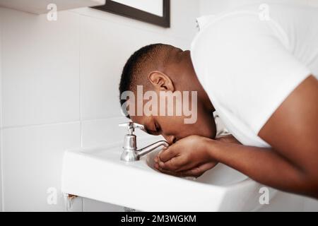 Jeder mag frischen Atem. Ein junger Mann, der sich zu Hause im Bad mit Wasser den Mund ausspült. Stockfoto