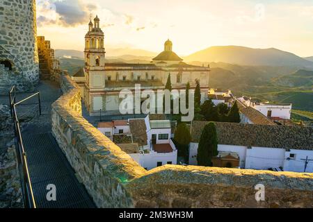 Spektakulärer Sonnenuntergang über den Bergen mit der alten Kirche und den weißen Häusern von Olvera in Cadiz. Stockfoto