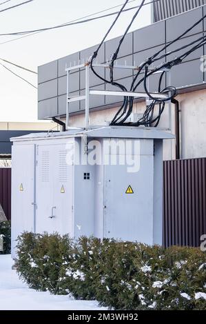 Eine elektrische Umspannstation in der Nähe eines Privathauses. Grauer Transformatorstand auf der Straße im Winter Stockfoto