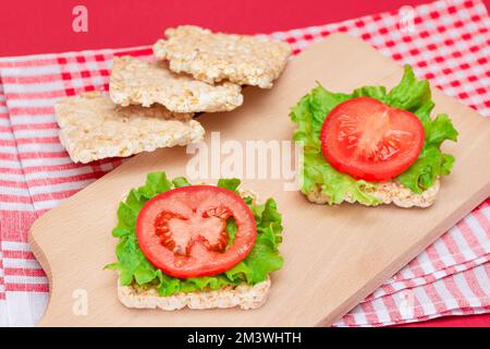 Reiskuchen-Sandwiches mit Tomaten und Salat auf Holzbrett. Einfaches Frühstück. Diät-Essen. Schnelle und gesunde Sandwiches. Knäckebrot mit leckerer Füllung. Gesunder Ernährungs-Snack Stockfoto