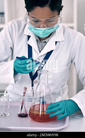 Lasst die Tests beginnen. Eine attraktive junge Wissenschaftlerin, die ein Experiment mit einer roten Flüssigkeit in einem Labor durchführt. Stockfoto