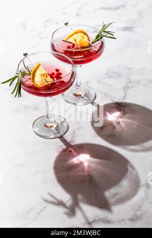 Zwei Weine aus Granatapfel mit Rosmarin und Zitrone auf weißem Marmorhintergrund, isoliert mit klaren Schatten in rauem Licht. Festliche Weihnachten Stockfoto