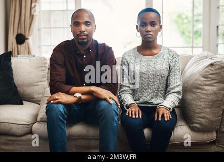 Waren mutig und unentschuldigt wegen unserer Liebe. Porträt eines jungen Paares, das ernst aussieht und zu Hause nebeneinander auf einem Sofa sitzt. Stockfoto