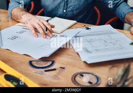 Design ist etwas, was er als Profi versteht. Ein nicht wiedererkennbarer männlicher Architekt, der mit Bauplänen in einem modernen Büro arbeitet. Stockfoto