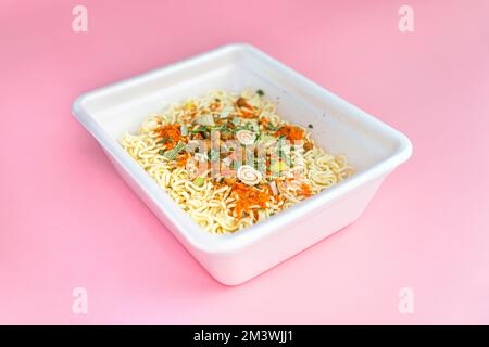 Getrocknete Instant-Nudeln in einer Plastikbox auf dem rosafarbenen Tisch. Draufsicht Stockfoto