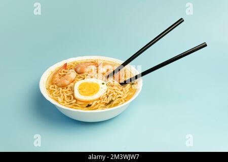 Würzige Suppe nach Thai-Art und Nudeln garniert mit Garnelen, genannt Tom Yum Goong auf weißer Schüssel mit Stäbchen, hergestellt mit Mama-Nudelgarnelen und Chili, heiß Stockfoto
