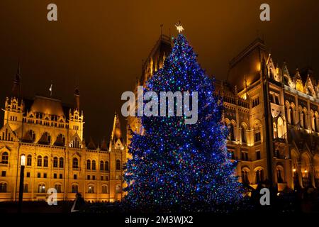 Budapest, Ungarn - 27.. November 2022: Ein beleuchteter weihnachtsbaum neben dem ungarischen Parlament bei Nacht. Stockfoto