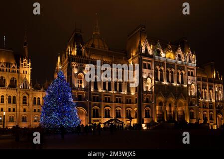 Budapest, Ungarn - 27.. November 2022: Ein beleuchteter weihnachtsbaum neben dem ungarischen Parlament bei Nacht. Stockfoto