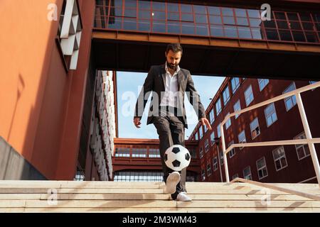 Bild eines Geschäftsmanns und Freispielers, der mit dem Ball auf der Straße Tricks macht. Konzept über Sport- und Geschäftsleute Stockfoto