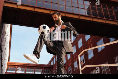 Bild eines Geschäftsmanns und Freispielers, der mit dem Ball auf der Straße Tricks macht. Konzept über Sport- und Geschäftsleute Stockfoto