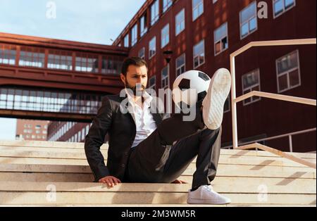 Bild eines Geschäftsmanns und Freispielers, der mit dem Ball auf der Straße Tricks macht. Konzept über Sport- und Geschäftsleute Stockfoto