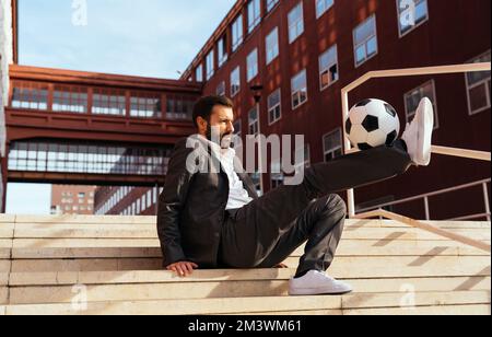 Bild eines Geschäftsmanns und Freispielers, der mit dem Ball auf der Straße Tricks macht. Konzept über Sport- und Geschäftsleute Stockfoto