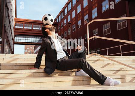 Bild eines Geschäftsmanns und Freispielers, der mit dem Ball auf der Straße Tricks macht. Konzept über Sport- und Geschäftsleute Stockfoto