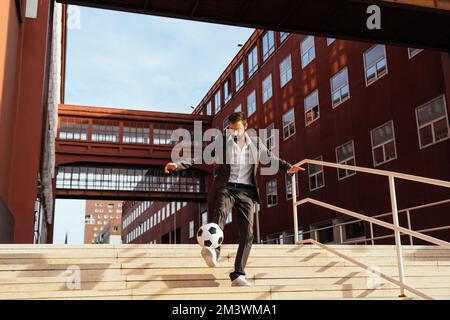 Bild eines Geschäftsmanns und Freispielers, der mit dem Ball auf der Straße Tricks macht. Konzept über Sport- und Geschäftsleute Stockfoto