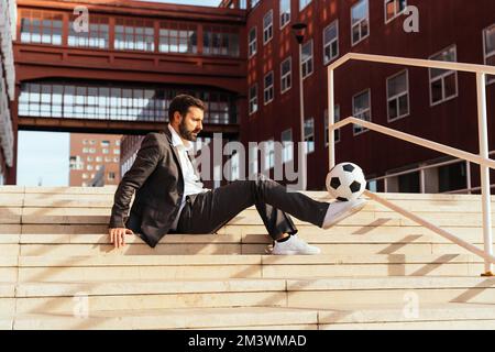 Bild eines Geschäftsmanns und Freispielers, der mit dem Ball auf der Straße Tricks macht. Konzept über Sport- und Geschäftsleute Stockfoto